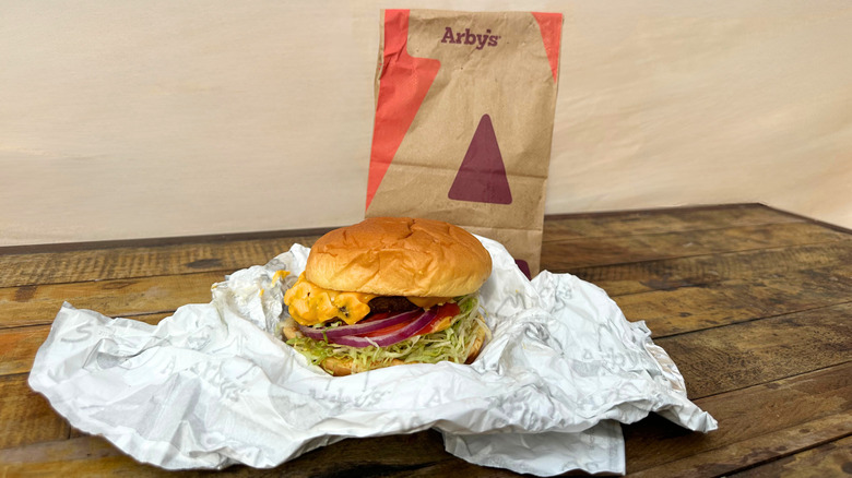 Deluxe Burger laid on a table with Arby's bag behind