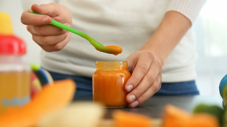 Parent spooning orange baby food from jar