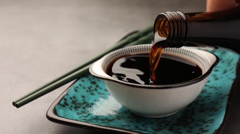 Soy sauce being poured into a bowl with chopsticks