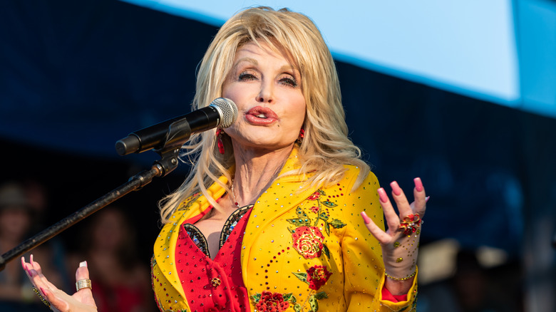 Dolly Parton in a yellow jacket singing into a microphone