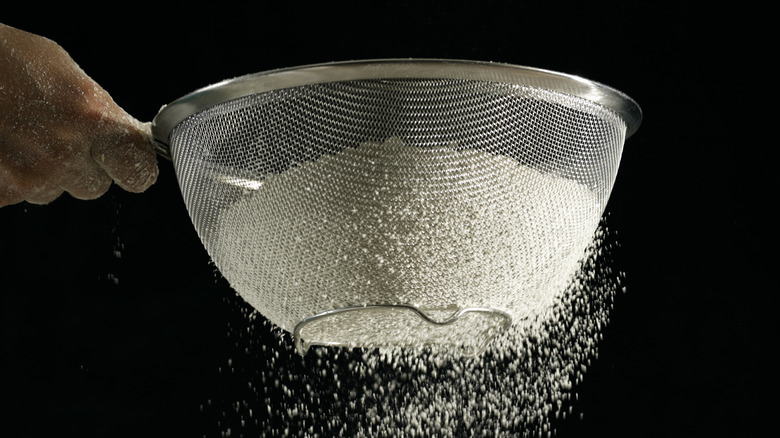 person sifting flour through mesh strainer