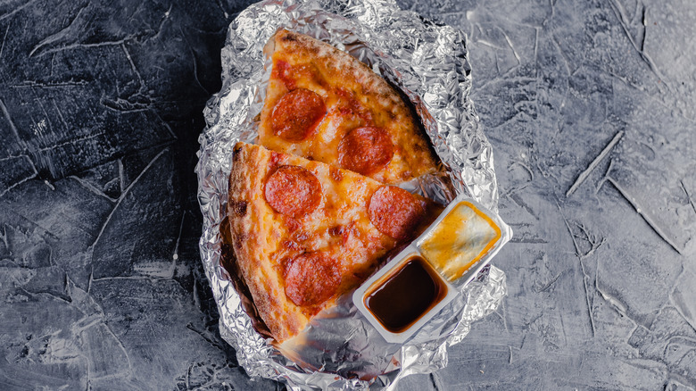 pepperoni pizza on aluminum foil with barbecue sauce packet