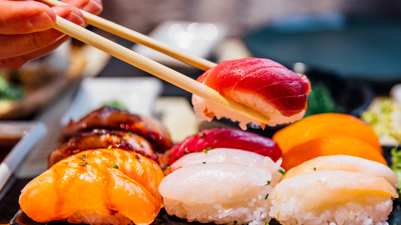 A hand using chop sticks to pick up one of several pieces of sushi