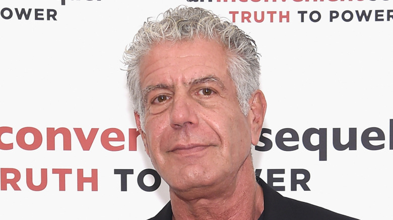 Anthony Bourdain wearing a black shirt and black blazer at an red carpet event.