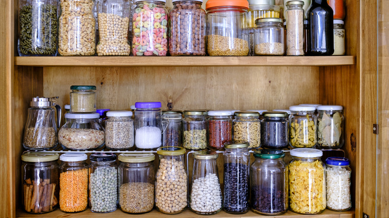 A pantry has multiple shelves filled with transparent jars.