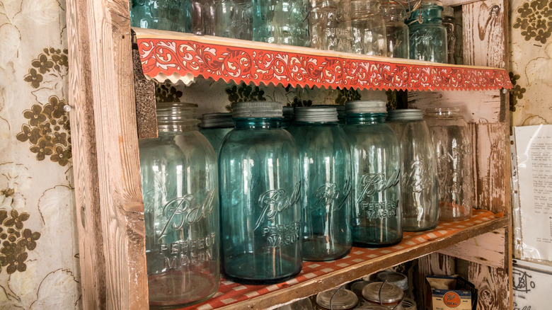 clear and teal mason jars on a wooden shelf with wallpaper.