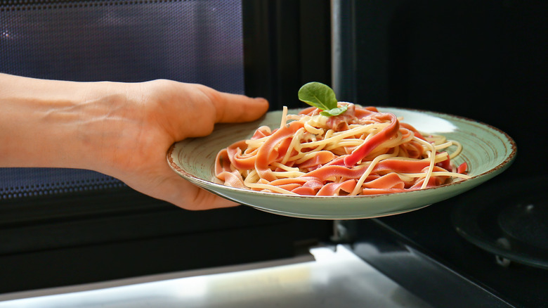 Person putting pasta in microwave