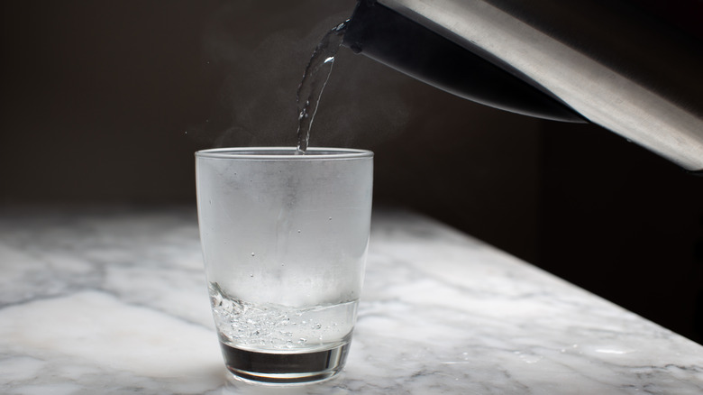 Glass being filled with hot water from a metallic pitcher