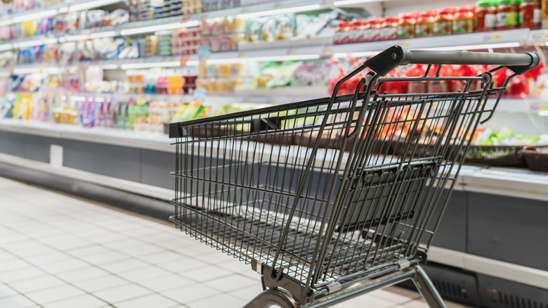 Empty black shopping cart inside a grocery store cooler aisle