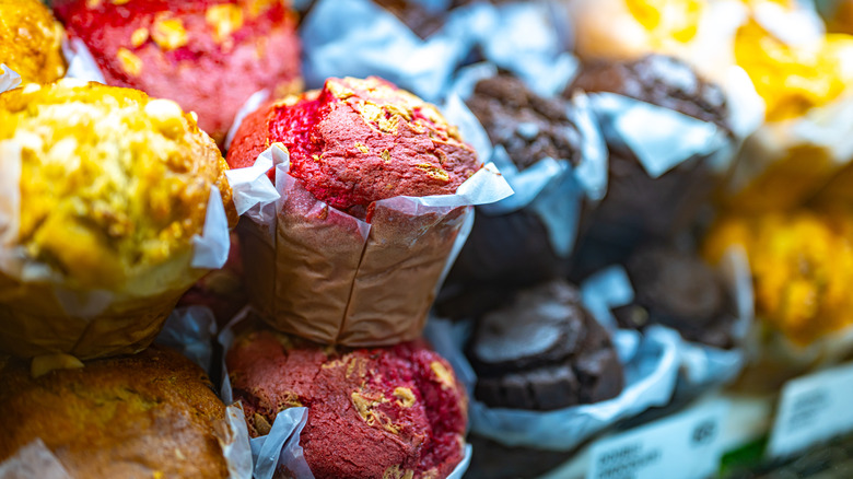 Assorted muffins of various colors for sale at a bakery counter