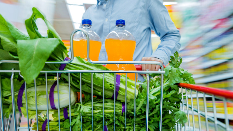 Pushing a shopping cart full of produce through blurry aisle of a grocery store