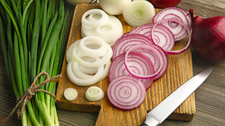 A cutting board and various onions
