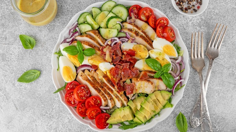 Cobb salad displayed on plate by dressing and silverware