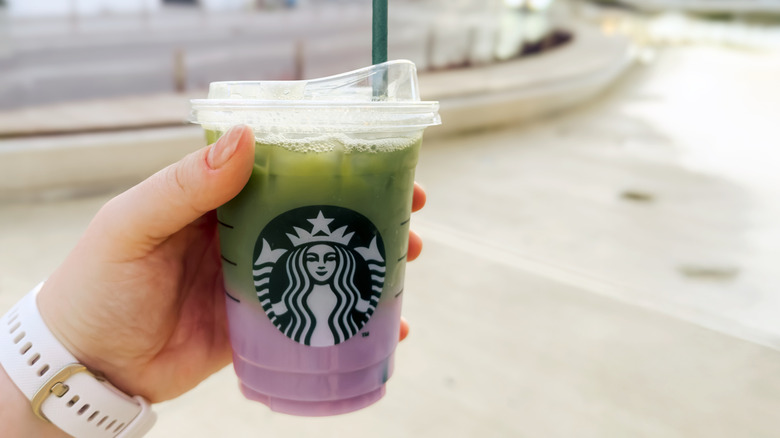 A hand holding a Starbucks drink with green and purple layers