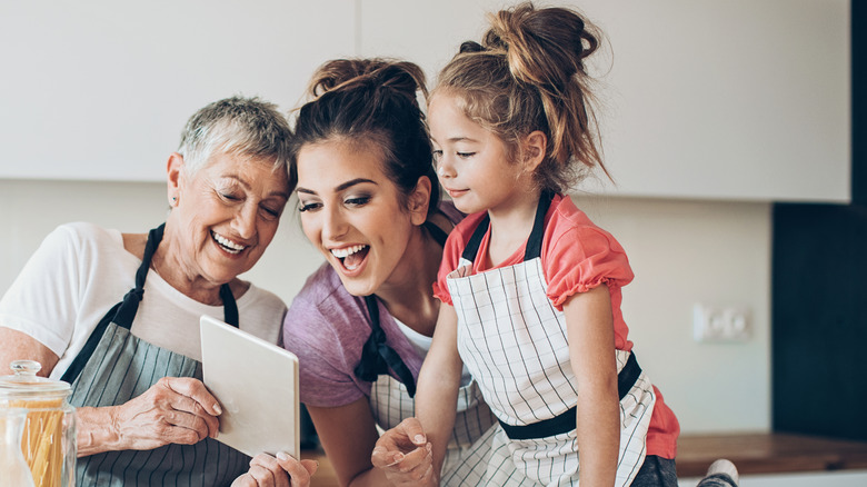 Three generations reading a recipe in aprons