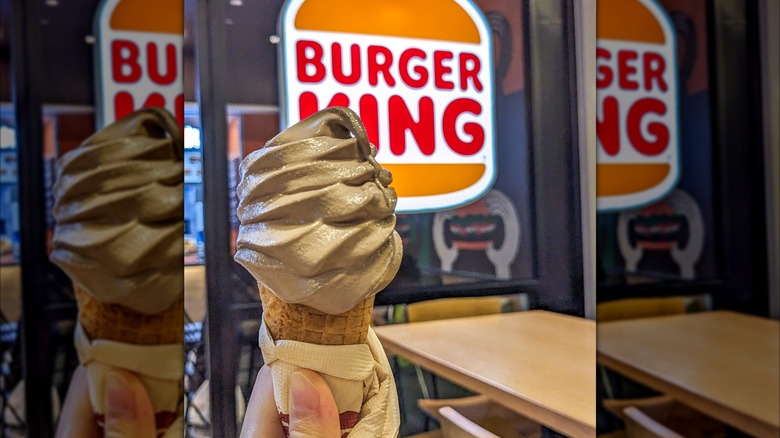 Hand holding Burger King Milo-flavored ice cream cones in front of Burger King sign