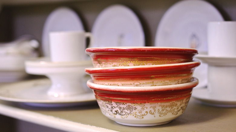 Three red and white bowls with gold detailing stacked in front of white plates