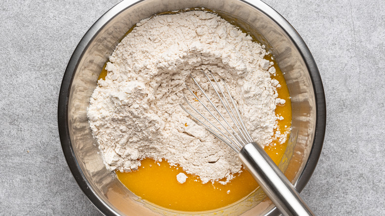 A French whisk in a silver metal mixing bowl with flour and wet mixture