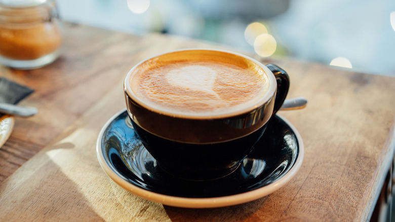 A black mug of a cappuccino on a wooden table at a coffee shop