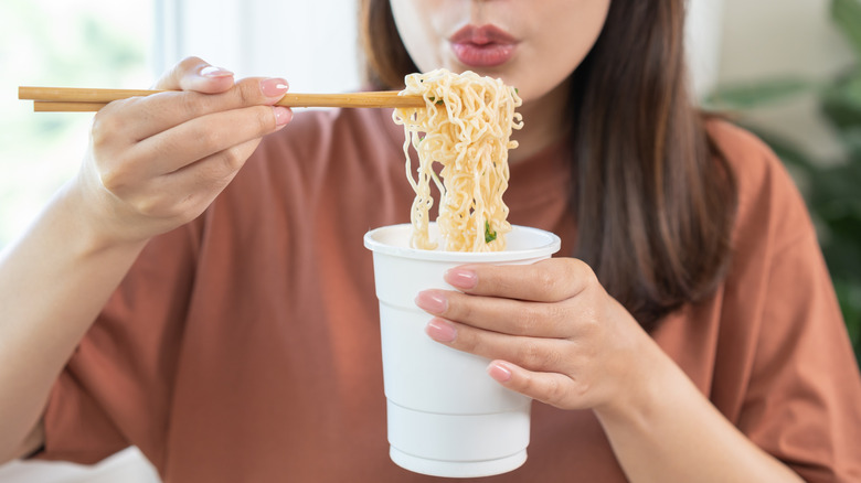 Woman eating instant ramen from cup with chopsticks
