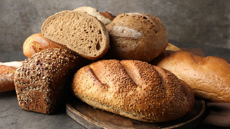 An assortment of bread loaves, both whole and halved, in a pile on a gray countertop.