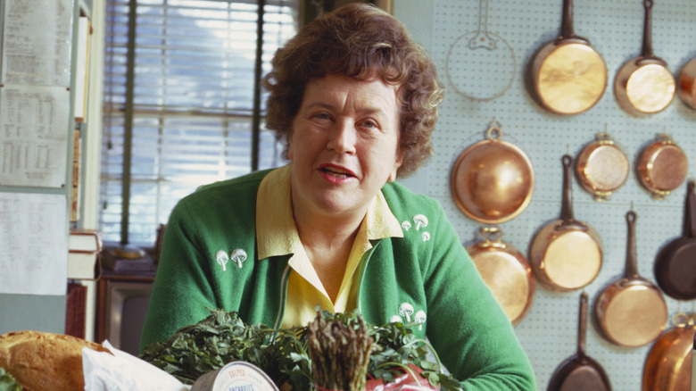 Julia Child in her kitchen surrounded by food and copper pans