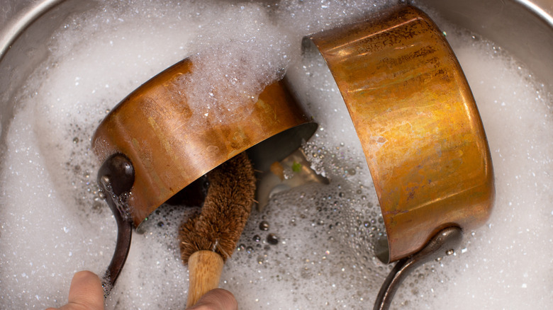 Copper pans soaking in soapy sink