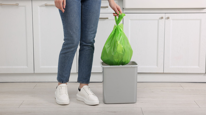 A person taking a green garbage bag out of a kitchen trash can