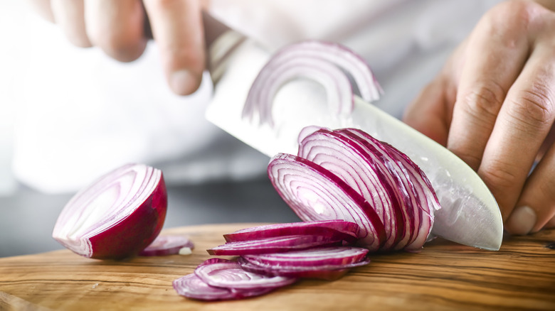 slicing red onion on wooden cutting board