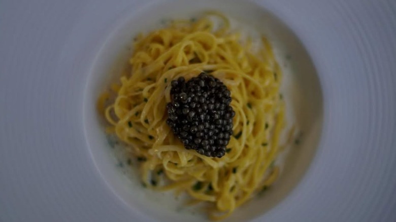 A bowl of pasta in cream sauce with caviar on top on a white plate