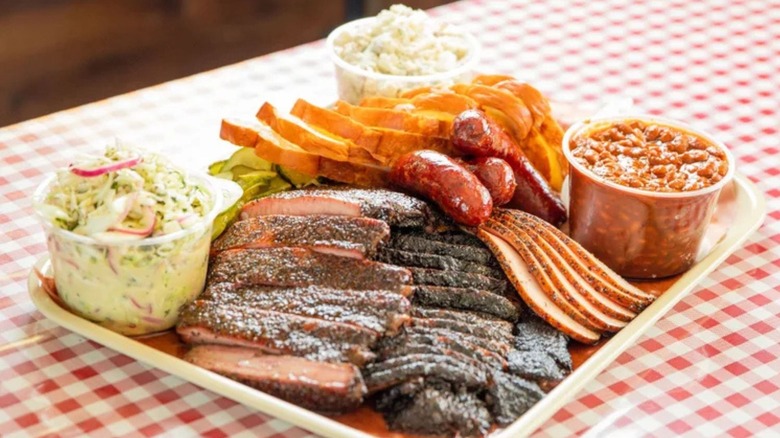 A large platter of meat and sides on a checkered tablecloth
