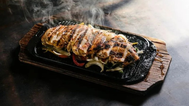 A wood board with a pan of sizzling fajitas on top of it with smoke
