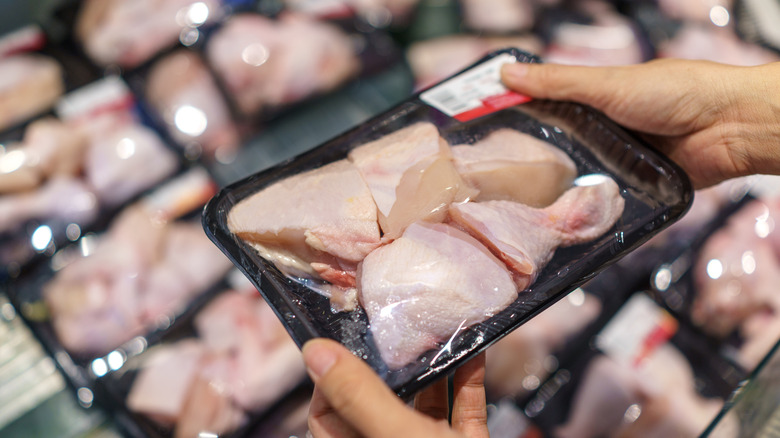 A person holding a pack of raw chicken in a supermarket