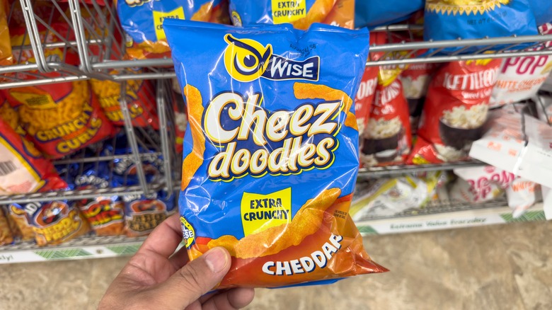 A person holds a bag of Cheez Doodles in the snack aisle