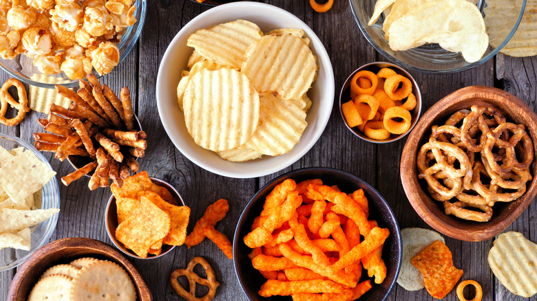 Overhead photo of a snack table filled with cheese puffs, chips, pretzels, and popcorn