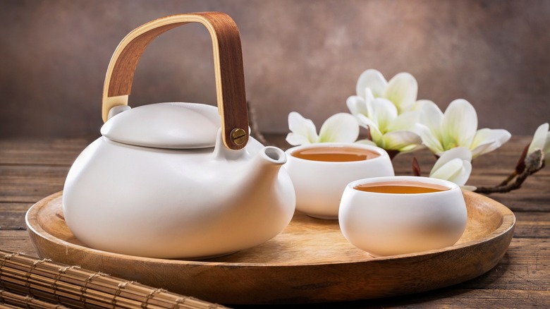 Tea in white cups next to a white teapot on a tray