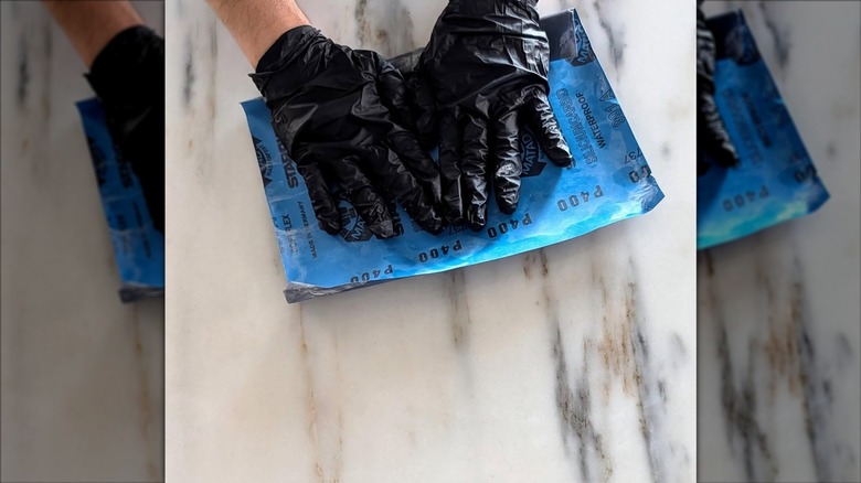 Gloved hands rubbing sandpaper over a marble surface