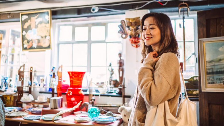 A cheerful woman shops for dishes and glassware at an antique store filled with items