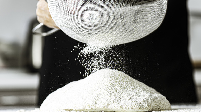 Sifting flour through a sieve onto a dough on the counter