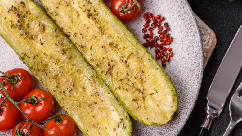 Cooked zucchinis sliced in half on a plate with cherry tomatoes