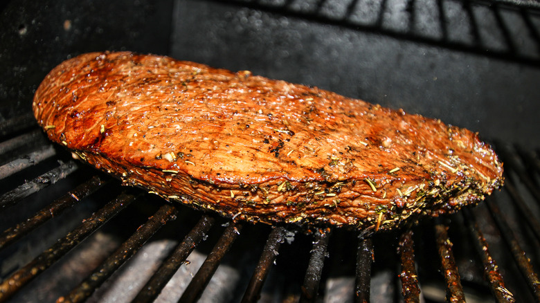 London broil cooking on a grill with iron grates
