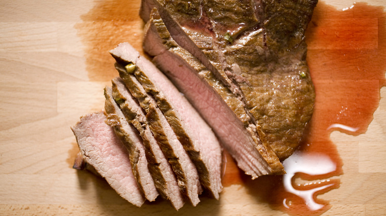 A flank steak prepared as London broil half sliced on a wood board with juices pooling around it