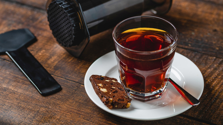 translucent cup of coffee with aeropress behind it