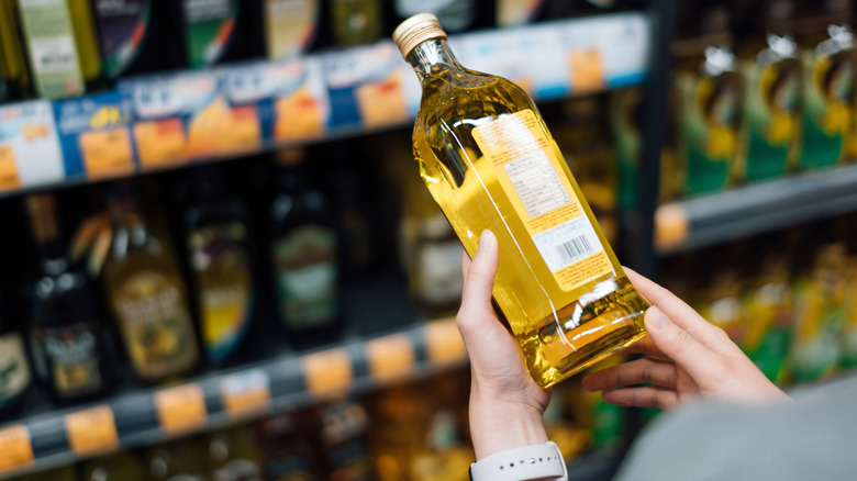 A woman inspecting a bottle of olive oil at a supermarket.