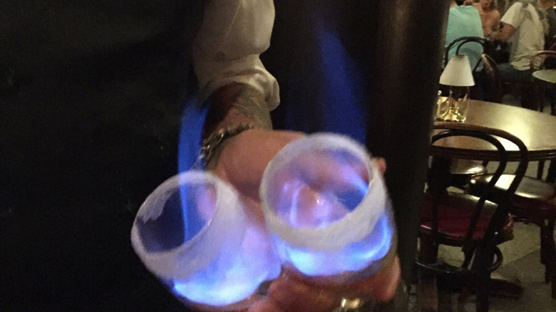 A server holding two sugar-rimmed glasses full of blue fire