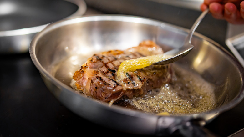 A steak cooking in a frying pan with butter being constantly spooned over the top
