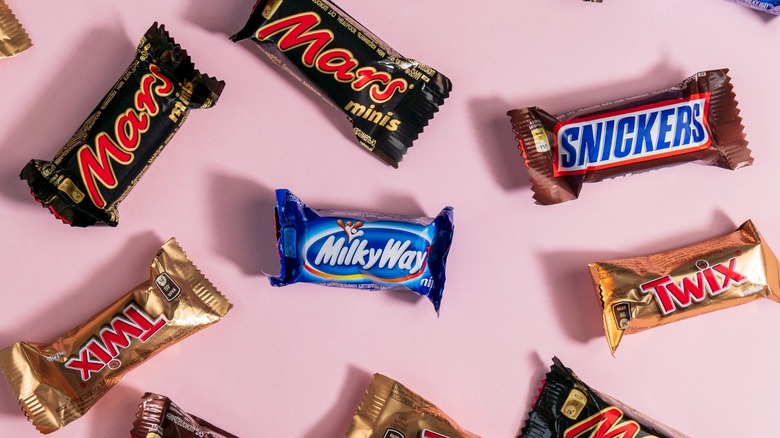 A variety of individually-wrapped mini candy bars on a pink background