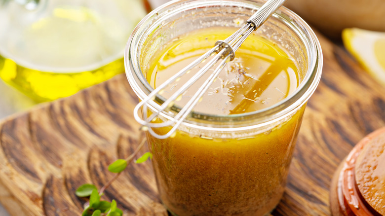 Salad dressing in jar with whisk and herbs