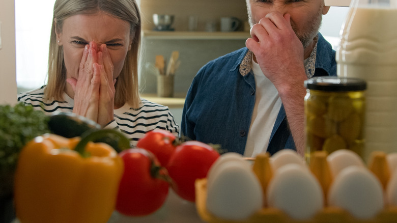 People holding their noses in front of a fridge