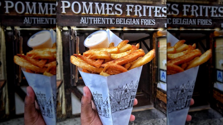 Hand holding french fries in front of Pommes Frites